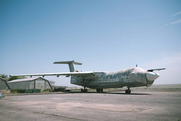 abandoned military aircraft on an empty airfield near the hangar against the blue sky. broken plane covered with a cloth on an empty airfield