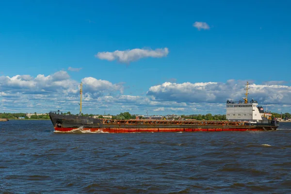 A barge floating along the sea along the shore. The sea barge is transporting goods of the appropriate destination. The sea is calm. The weather is sunny.