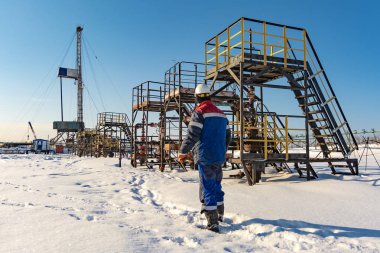 Petrolcü, petrol kuyuları üreten boyunca Kuzey alan oluyor. Arka plan bir sondaj kulesi. Kış. Güneşli gün.