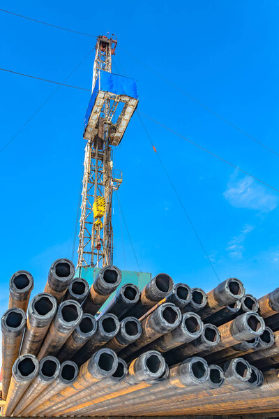 Drill pipes in the foreground. In the background is a mobile drilling rig for drilling oil and gas wells. Background - blue sky with clouds.
