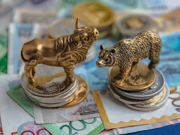 The bronze bull and bear figurines are arranged with paper money and metal coins. Blur background. Symbol and concept of trading on the stock exchange.