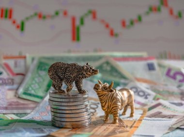 Kağıt para ve grafiklerin arka planına karşı metal sikkelerin yanında bir boğa ve bir ayının bronz figürleri. Bulanıklık arka plan ve perspektif. Borsa ve borsa işlemlerinin kavramı ve sembolü.