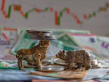 Kağıt para ve grafiklerin arka planına karşı metal sikkelerin yanında bir boğa ve bir ayının bronz figürleri. Bulanıklık arka plan ve perspektif. Borsa ve borsa işlemlerinin kavramı ve sembolü.