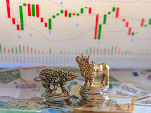 Bronze figures of a bull and a bear near metal coins against the background of paper money and charts. Blur background and perspective. Concept and symbol of stock exchange and stock trading.