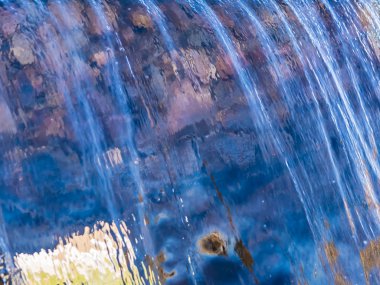 Düşen bir su duvarının oluşturduğu bulanık görüntü. Şelalede çeşitli su figürleri. Çok renkli soyut aqua görüntünün yarı saydam arka planı.