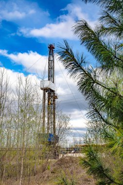 Petrol ve gaz sondaj Rig odak arka planda. Ön planda, baharda Genç ağaçlar odak dışında. Sibirya 'da bahar doğası. Güneşli gün.