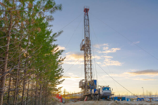 Drilling a deep well mobile drilling rig in an oil and gas field. The field is located in the Far North in the taiga. Beautiful dramatic sunset sky in the background.