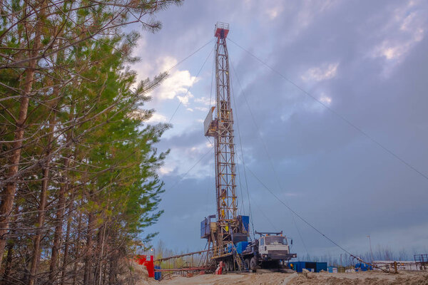 Drilling a deep well mobile drilling rig in an oil and gas field. The field is located in the Far North in the taiga. Beautiful dramatic sunset sky in the background.