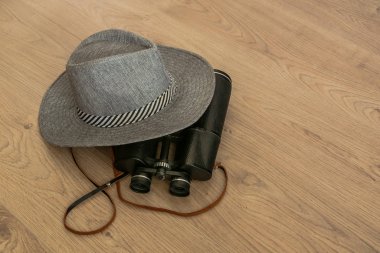 Geniş kenarlı gri şapka ve dürbün, seyahat sembolleri olarak. Ahşap sarımsı arka plan. Tasarımcı için hazırlık. Kopyalama alanı.