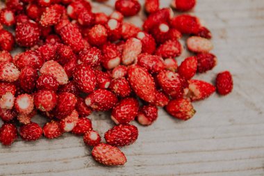 Birkaç olgun yabani çilek çilek ahşap bir masaya serpilir. Sağlıklı bir diyet için vitamin içeren kırmızı meyveler.