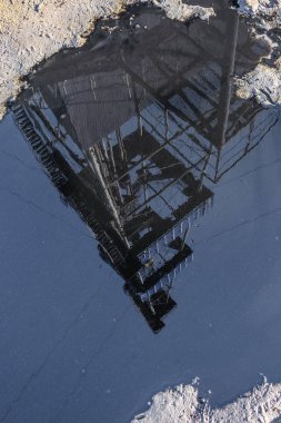 Drilling rig reflection in a puddle of oil. The concept of pollution of the Earth's surface during oil and gas production Ecological disaster due to the activities of oil companies. clipart