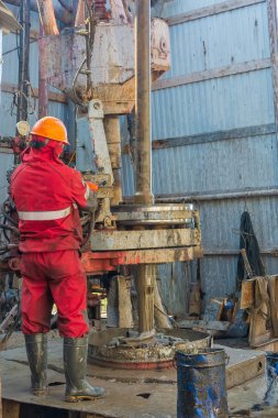 Kırmızı üniformalı, miğferli ve gözlüklü matkapçı. Petrol kuyusuna indirmek için matkap borularını vidalamak ve delmeye devam etmek için hidrolik anahtar kullanıyor. Çalışan insan kavramı.