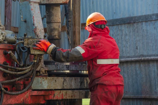 Kırmızı üniformalı, miğferli ve gözlüklü matkapçı. Petrol kuyusuna indirmek için matkap borularını vidalamak ve delmeye devam etmek için hidrolik anahtar kullanıyor. Çalışan insan kavramı.