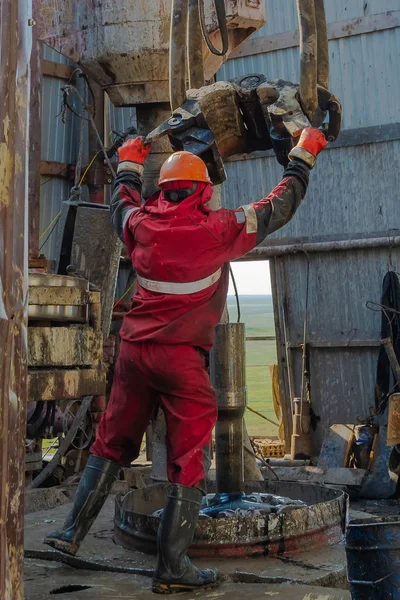 赤いユニフォーム ヘルメットとゴーグルで作業ドリラー 彼はエレベーターの助けを借りて 油田からそれらを持ち上げ その掘削を続けるためにドリルパイプをハングアップします 働く人の概念 — ストック写真
