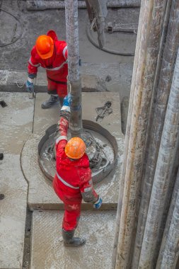 Kırmızı üniformalı, kask ve gözlüklü iki sondajcı, sondaj dan sonra bir petrol kuyusundan kaldırdıktan sonra matkap boruları tökezler. Çalışan bir kişi kavramı.