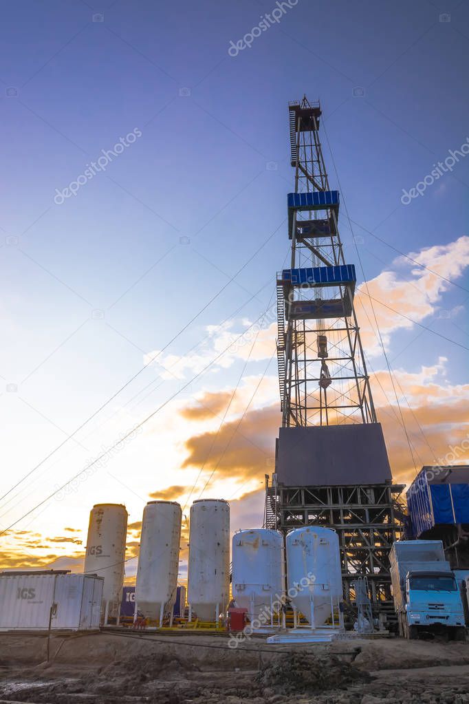 Drilling rig with a tower tower. Downstairs is the drilling equipment. A deep well is being drilled in the northern field for oil and gas production. Summer polar night. Beautiful sky with backlit clouds.
