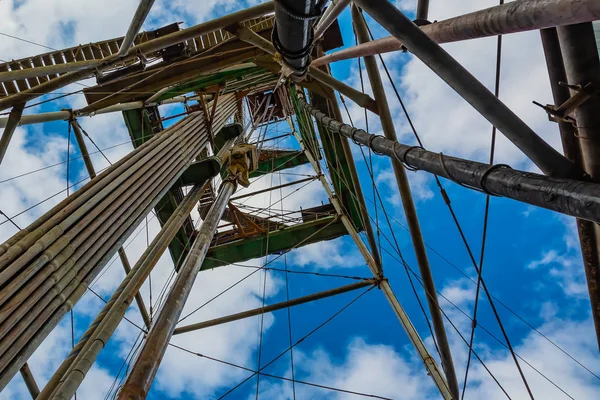 The location of the equipment inside the drilling rig for oil and gas drilling. Vertical stand drill pipes. Lifting system. Bottom-up view. Blue cloudy sky.