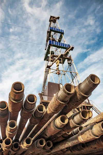 Ön planda matkap boruları vardır. Arka planda petrol ve gaz üretimi için kuzey alanında sondaj kuyuları için bir sondaj kulesi bulanık bir görüntüdür. Yaz günü. Mavi bulutlu gökyüzü.