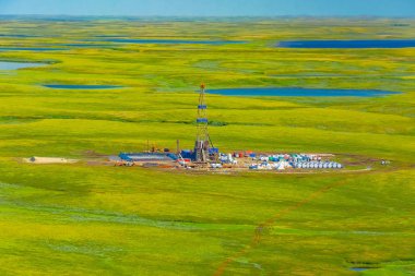 Drilling rig and equipment at an oil field in the northern tundra. Top view from a helicopter. Green summer tundra with lakes beyond the Arctic Circle. clipart