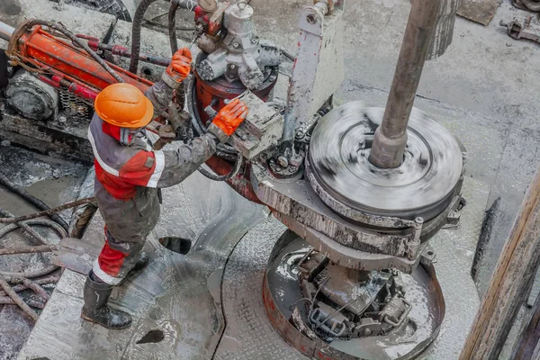 Kırmızı üniformalı, miğferli ve gözlüklü matkapçı. Petrol kuyusuna indirmek için matkap borularını vidalamak ve delmeye devam etmek için hidrolik anahtar kullanıyor. Çalışan insan kavramı.