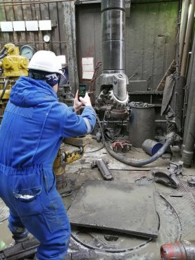 Bir matkap ucu uzmanı bir petrol ve gaz kuyusundan çıkarılan parçanın durumunu inceliyor. Mühendis mavi bir tulum ve beyaz bir şapka giyiyor..