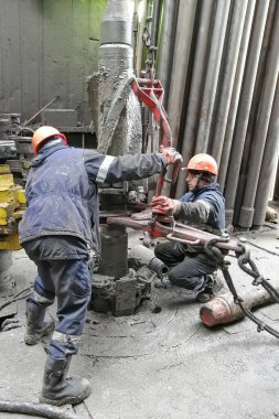 Novy Urengoy / Rusya - Mayıs 03 2020: İki sondaj işçisi, güç anahtarı kullanarak sondaj ve sondaj aletini kırmanın yanı sıra petrol ve doğalgaz üretimi kuyusuna akıtıyorlar.