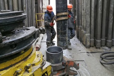 Novy Urengoy / Rusya - Mayıs 03 2020: İki sondaj işçisi, güç anahtarı kullanarak sondaj ve sondaj aletini kırmanın yanı sıra petrol ve doğalgaz üretimi kuyusuna akıtıyorlar.