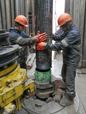 Novy Urengoy / Rusya - Mayıs 03 2020: İki sondaj işçisi, güç anahtarı kullanarak sondaj ve sondaj aletini kırmanın yanı sıra petrol ve doğalgaz üretimi kuyusuna akıtıyorlar.