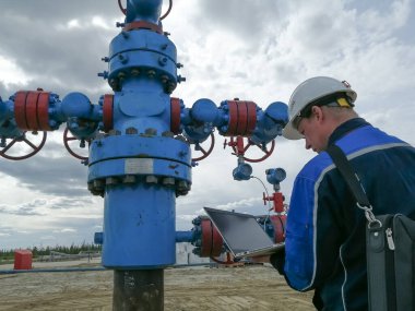 Novy Urengoy / Rusya - 29 Mayıs 2020: Bir petrol ve gaz üretim uzmanı, bir dizüstü bilgisayar kullanan bir jeolog, petrol ve gaz üretiminin teknolojik parametrelerini ve modellerini bir kuyudan belirler. Çeşmeye manometreler ve termometreler yerleştirildi