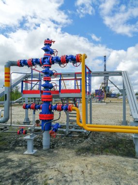 Kuzey bölgesinde gaz kuyuları üreten boru hattı manifoltları. Yüksek basınçlı kapı valf el tekerlekleri, boru hatları. Arka planda bir sondaj kulesi var. Bulanık uzak nesneler.