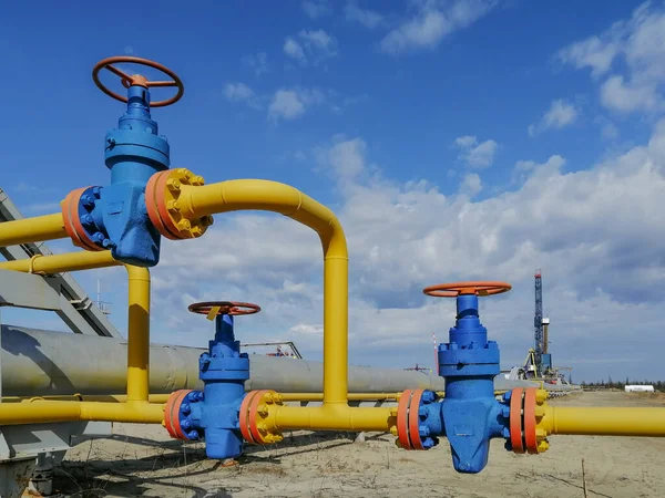 Boru hattı tesisatları ve sahada gaz kuyuları üretme manifoltları. Yüksek basınçlı valfler için el tekerlekleri. Arka planda bir sondaj kulesi var. Bulanık uzak nesneler.