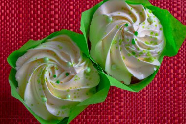 Beyaz kremalı iki kekin tatlı tatlısı. Yeşil kağıt konteynır. Kırmızı hasır geri.