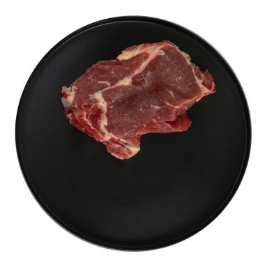 İzole görüntü. Taze biftek siyah yuvarlak bir tabakta yatıyor. Yukarıdan bak. Gıda bileşiminin oluşumu için çalışma