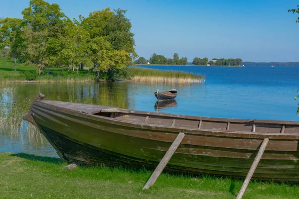 Güneşli bir yaz gününde Onega Gölü 'ndeki Kizhi adasında manzara. Ön plandaki gölde büyük ahşap bir tekne. Arka planda gölde yüzen bir tekne, ağaçlar ve göl genişliyor.