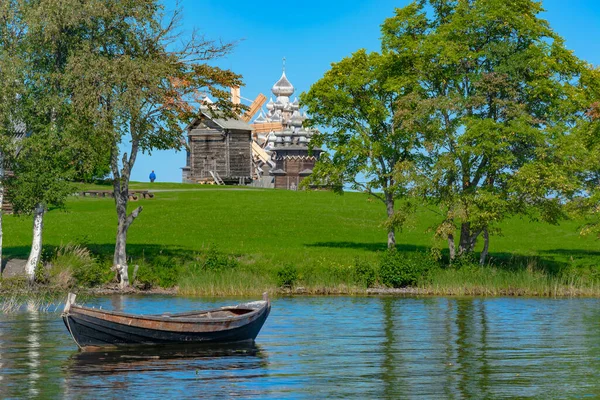 Güneşli bir yaz gününde Onega Gölü 'ndeki Kizhi adasında manzara. Ön planda ahşap balıkçı teknesi. Arka planda eski bir ahşap değirmen, bir tapınak ve bir kilise var.