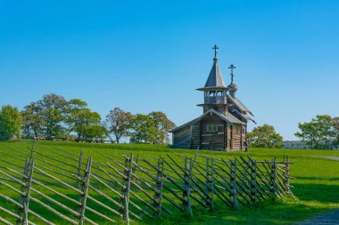 Güneşli bir yaz gününde Onega Gölü 'ndeki Kizhi adasında manzara. Yeşil çayır. Ön planda tahta çit var. Eski ahşap bir kilisenin arka planı.