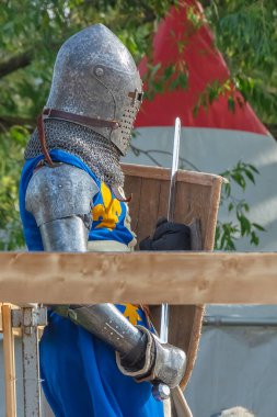 Ağır ortaçağ zırhlı bir şövalye kılıçlı bir rakiple savaşmaya hazırlanıyor. Demir bir miğfer ve kalkan tarafından korunuyor. Ortaçağ Avrupa şövalye turnuvalarının tarihi yeniden yapılandırması