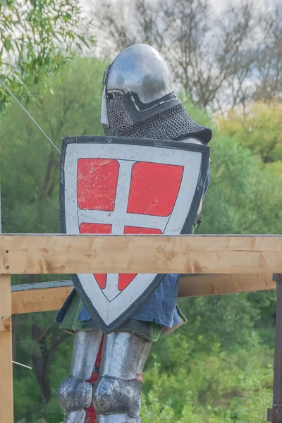 A knight in heavy medieval armor prepares to fight an opponent with swords. Protected by an iron helmet and shield. Historical reconstruction of medieval European knightly tournaments