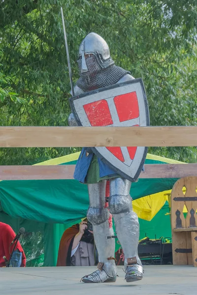 A knight in heavy medieval armor prepares to fight an opponent with swords. Protected by an iron helmet and shield. Historical reconstruction of medieval European knightly tournaments