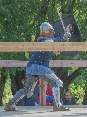 Tver / Rusya - 29 Eylül 2020: Ağır ortaçağ zırhlı bir şövalye kılıçlarla bir rakiple savaşmaya hazırlanıyor. Demir bir miğfer ve kalkan tarafından korunuyor. Ortaçağ Avrupa şövalye turnuvalarının tarihi yeniden yapılandırması