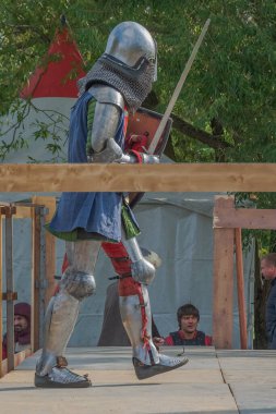 Tver / Rusya - 29 Eylül 2020: Ağır ortaçağ zırhlı bir şövalye kılıçlarla bir rakiple savaşmaya hazırlanıyor. Demir bir miğfer ve kalkan tarafından korunuyor. Ortaçağ Avrupa şövalye turnuvalarının tarihi yeniden yapılandırması