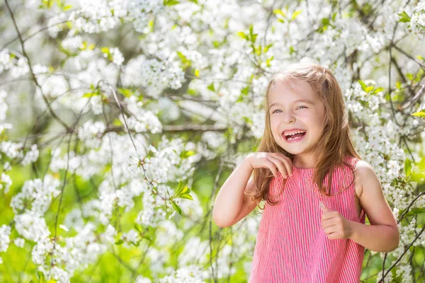 Lycklig liten flicka i körsbärsblom trädgård — Stockfoto