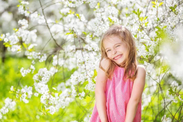 Счастливая маленькая девочка в саду цветущей сакуры — стоковое фото