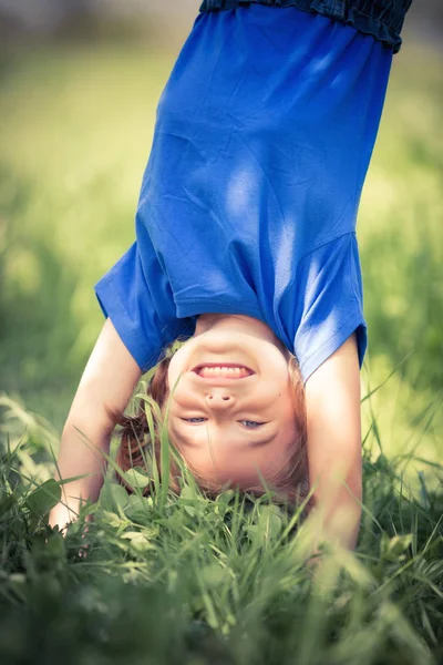 Happy little girl standing upside down on grass in summer park — Stock Photo, Image