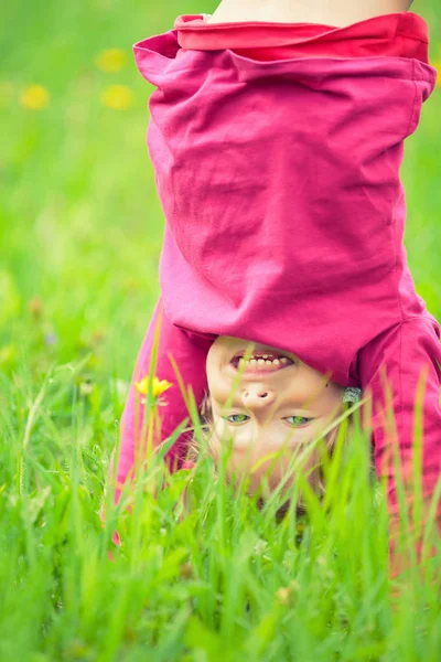 Happy little girl standing upside down on grass in summer park — Stock Photo, Image