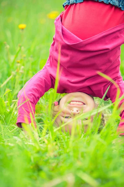 Happy little girl standing upside down on grass in summer park — Stock Photo, Image
