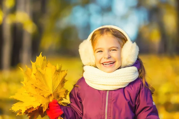 Happy little girl in earflaps with autumn leaves — Stock Photo, Image