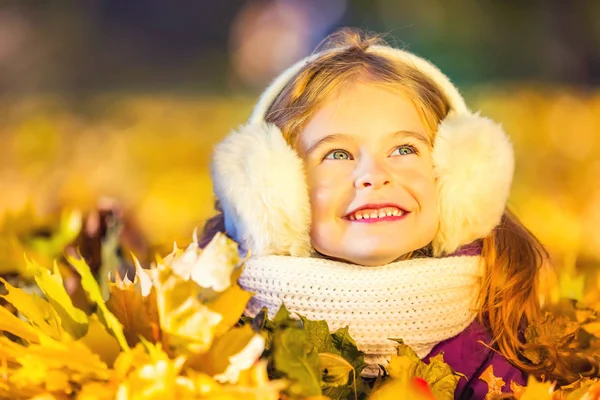 Menina em earflaps brincando com folhas de outono — Fotografia de Stock