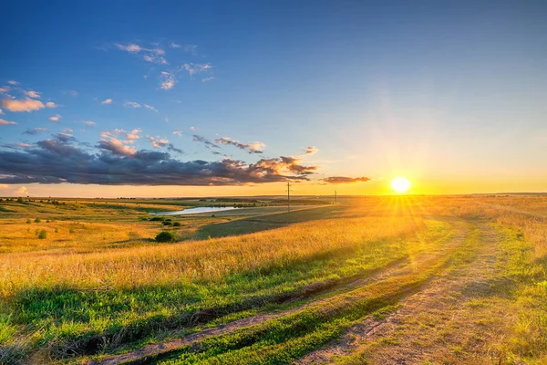 Paesaggio rurale con strada sterrata e campo di grano al bellissimo tramonto estivo — Foto Stock