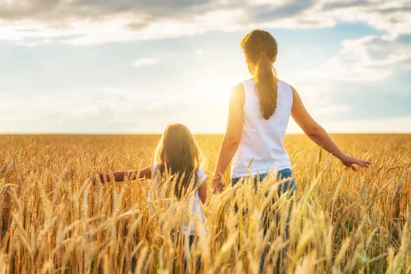 Mujer joven y su hija caminando en el campo de trigo dorado en el día soleado . — Foto de Stock